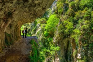 Sendero junto al precipicio mientras dos personas miran el paisaje montañoso con multitud de vegetación. Foto de Gabriel González