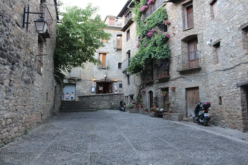 Placita empedrada y fachada con vegetación en Aínsa